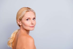 Attractive blonde woman in her 60s looks over her shoulder, pondering whether to continue Botox or schedule a brow lift